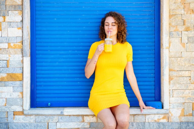 Femme buvant un jus de fruit devant un volet roulant bleu